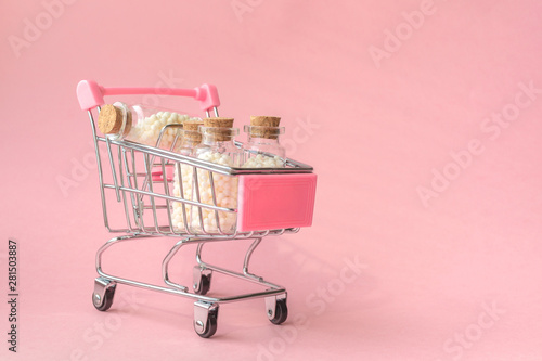 Tiny shopping cart with homeopathic preparations in cans. Homeopathic natural medicines without chemicals in banks in shopping cart on pink background