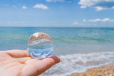 The glass round ball on the hand reflects the beach in the summer