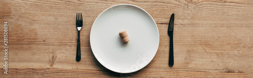 panoramic shot of plate with cork and cutlery on wooden surface