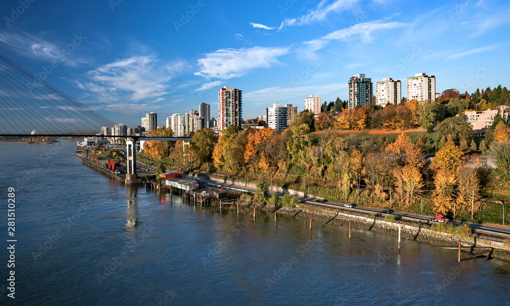  New Westminster City the slopes of the Fraser River, painted with autumn colors, Sky Train Bridge and a  road against the background of a bright sky with white clouds