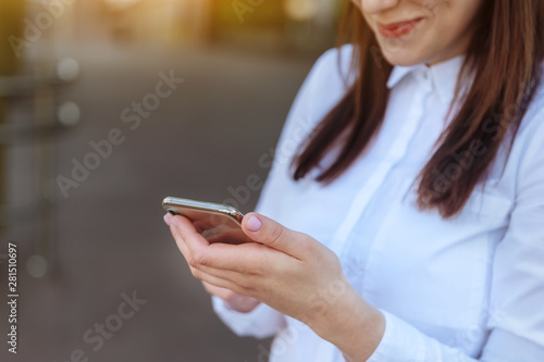 Portrait young business woman wearing white shirt using smartphone out doors. Female reading sms message in working process. © Volha