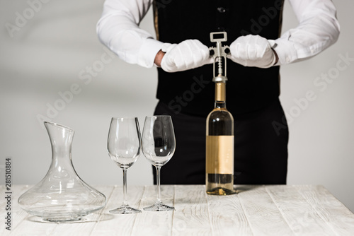 partial view of waiter in white gloves opening bottle of wine with corkscrew photo