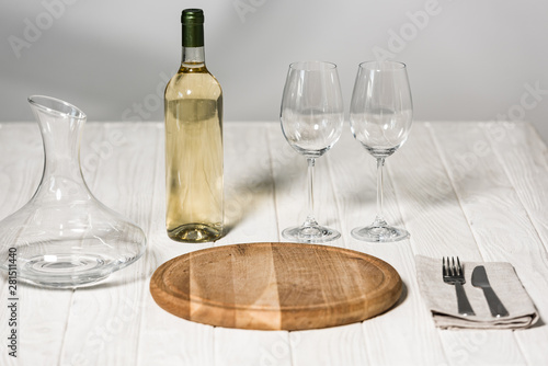 bottle of wine, jug, wine glasses, cutlery and cutting board on wooden surface in restaurant