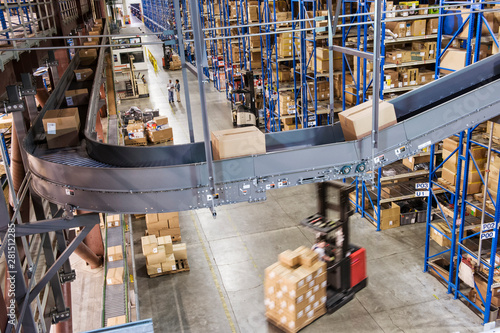 View of conveyor belt, racks and forklift trucks in distribution warehouse