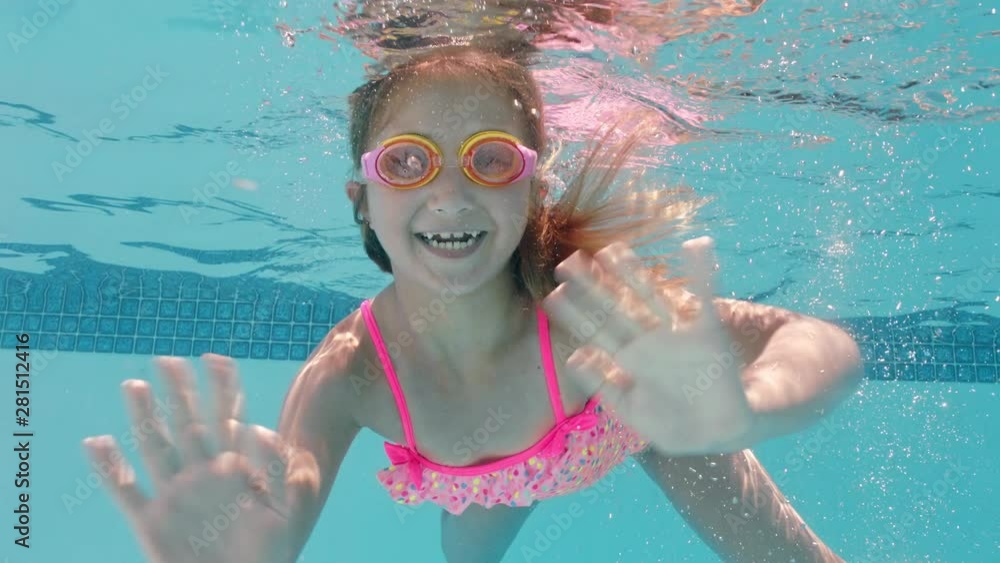 happy little girl swimming underwater in pool smiling waving hand ...