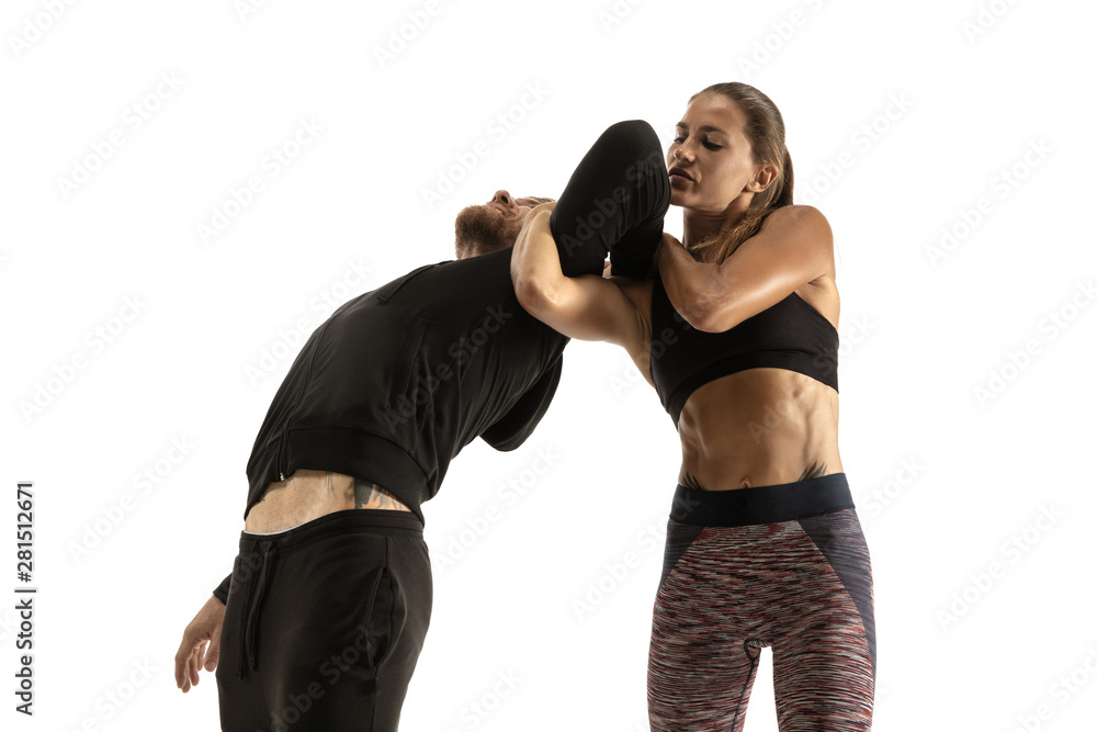 Man in black outfit and athletic caucasian woman fighting on white studio background. Women's self-defense, rights, equality concept. Confronting domestic violence or robbery on the street.