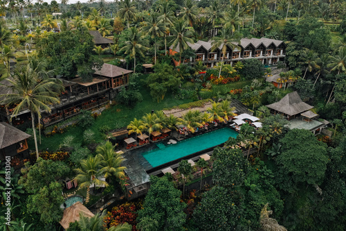 Aerial view of luxury hotel with straw roof villas and pools in tropical jungle and palm trees. Luxurious villa, pavilion in forest, Ubud, Bali