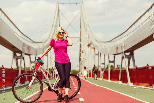Back view of young slim woman standing at bicycle on bridge background. Active lifestyle and vacations concept.