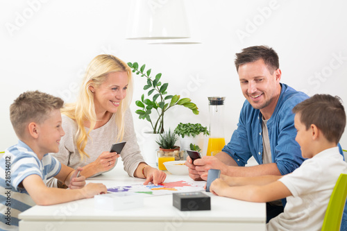 Happy young family playing card game at dining table at bright modern home. Spending quality leisure time with children and family concept. Cards are generic and debranded.