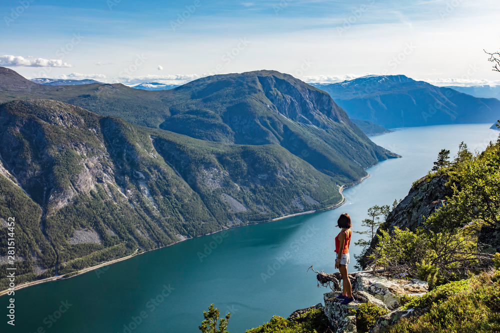 Female traveler enjoying the beautiful scenery at the top of a fjord in Norway during a hike in summer