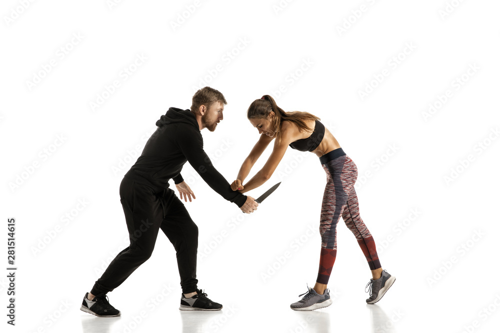 Obraz premium Man in black outfit and athletic caucasian woman fighting on white studio background. Women's self-defense, rights, equality concept. Confronting domestic violence or robbery on the street.