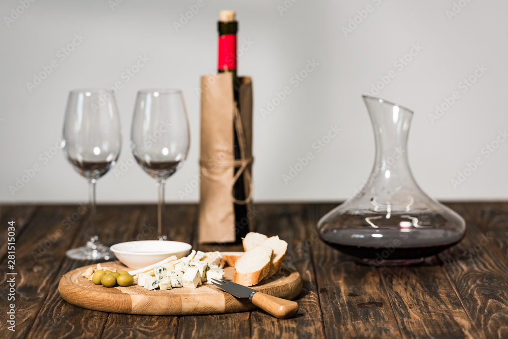 bottle of wine, wine glasses, jug, cheese, olives and bread on wooden surface