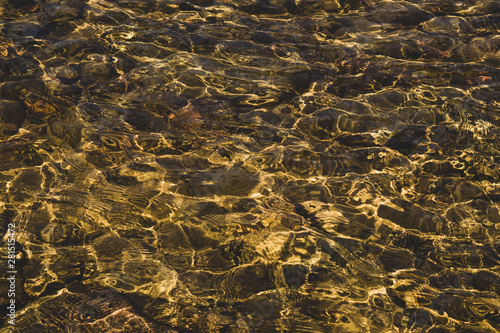 Shiny transparent water. clear water with pebbles and stone on the bottom. shining reflections of sun rays and ripples on the water