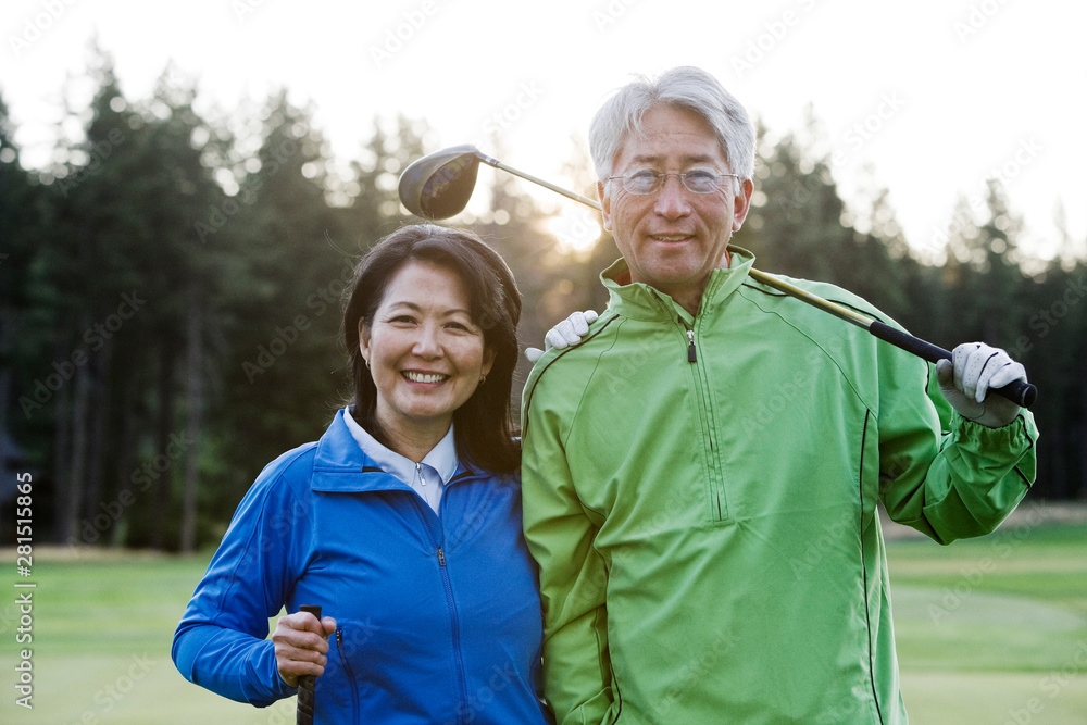 © Mint Images - Portrait of smiling couple with golf club standing on golf course