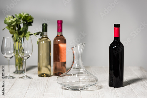 bottles of wine, wine glases, vase with green plants and jug on wooden surface
