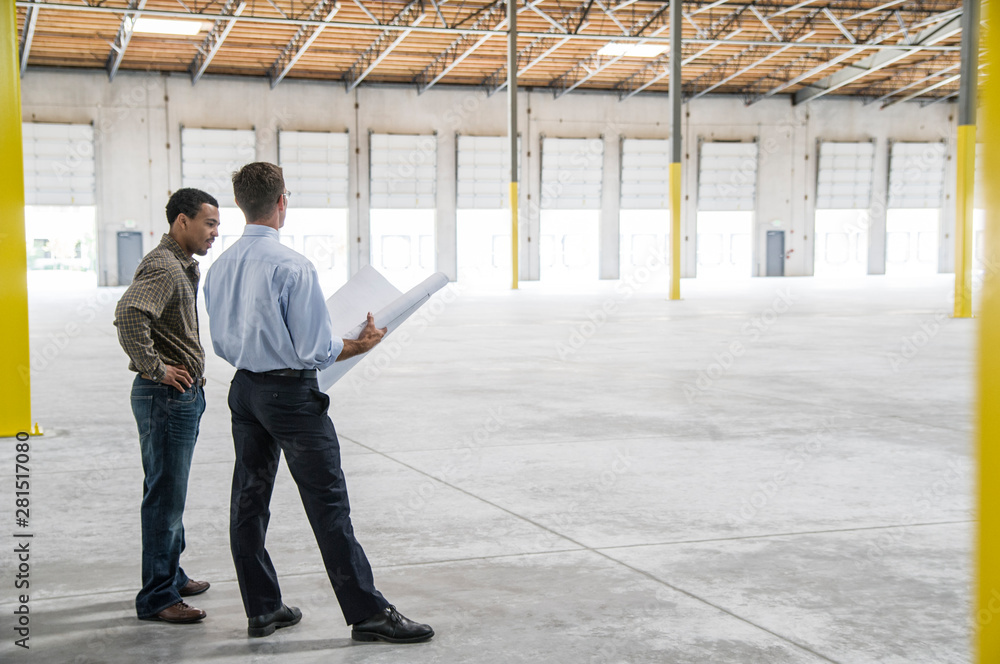 © Mint Images - Owner and architect talking over blueprints in warehouse