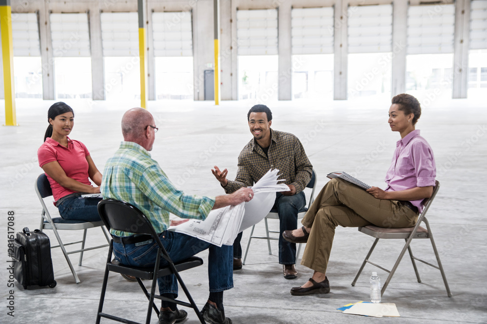 Architects talking over blueprint while sitting in warehouse Architects talking over blueprint while sitting in warehouse