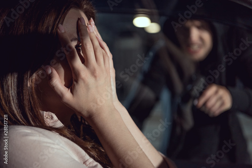 thief pointing gun at woman sitting in car at night