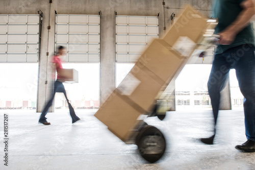 Man pushing hand truck loaded with cardboard box in warehouse