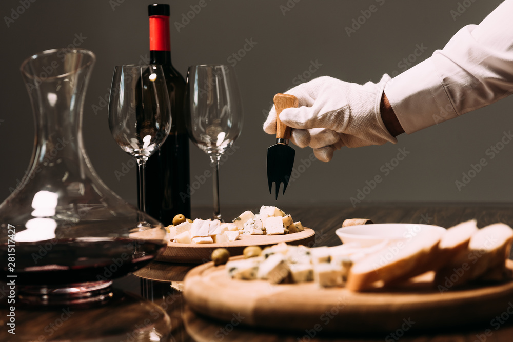 cropped view of waiter in white glove holding cheese fork near table with food and wine cropped view of waiter in white glove holding cheese fork near table with food and wine