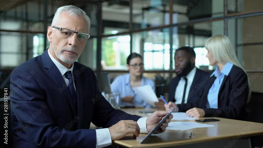 Mature businessman thinking of decision looking tablet, managers discussing plan Mature businessman thinking of decision looking tablet, managers discussing plan