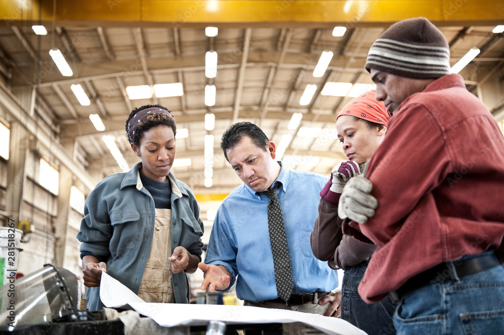 Manager and workers talking over blueprint in factory