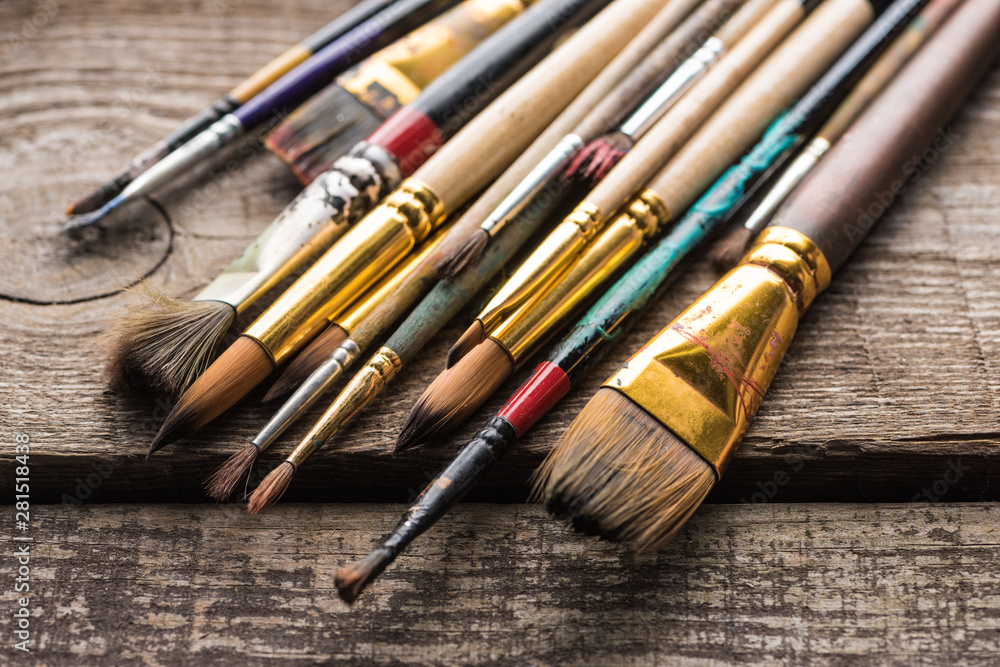 Fototapeta premium close up view of old paintbrushes on wooden brown surface