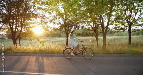 Young beautiful female riding bicycle on countryside road and smiling, feeling happy and relaxed, weekend leisure