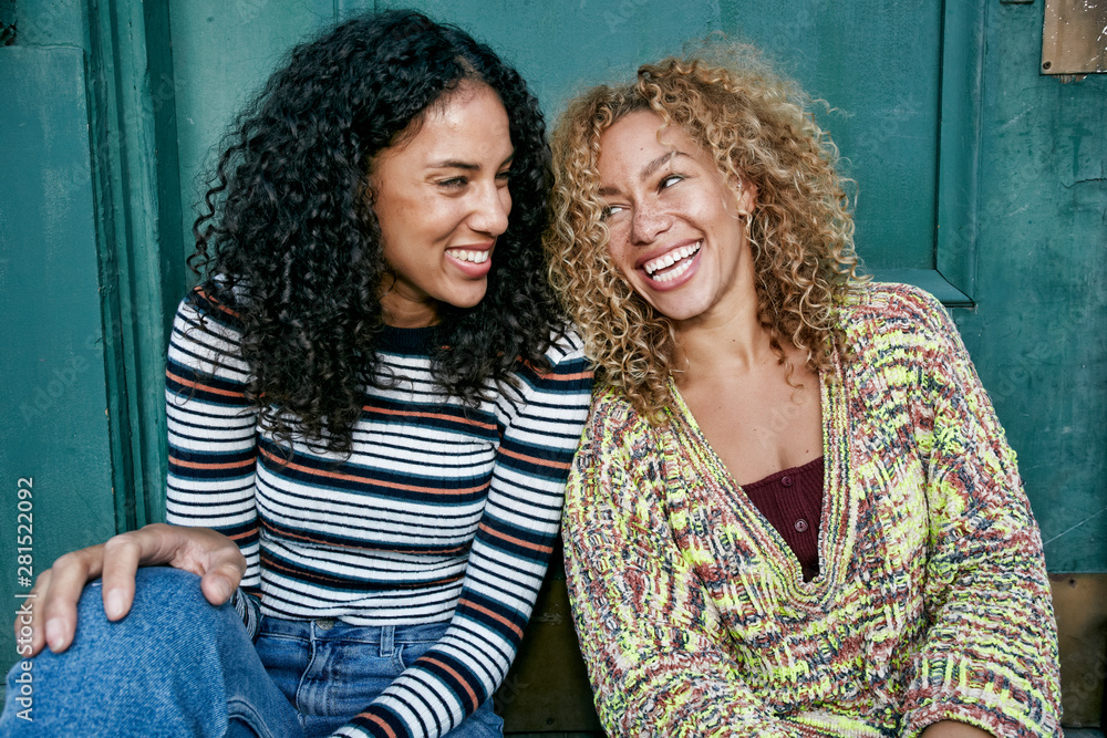 Smiling friends with curly hair sitting outdoors Smiling friends with curly hair sitting outdoors