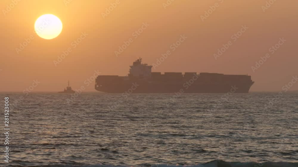 Beautiful shot of a huge cargo ship travelling across water with the sun setting in the background Beautiful shot of a huge cargo ship travelling across water with the sun setting in the background