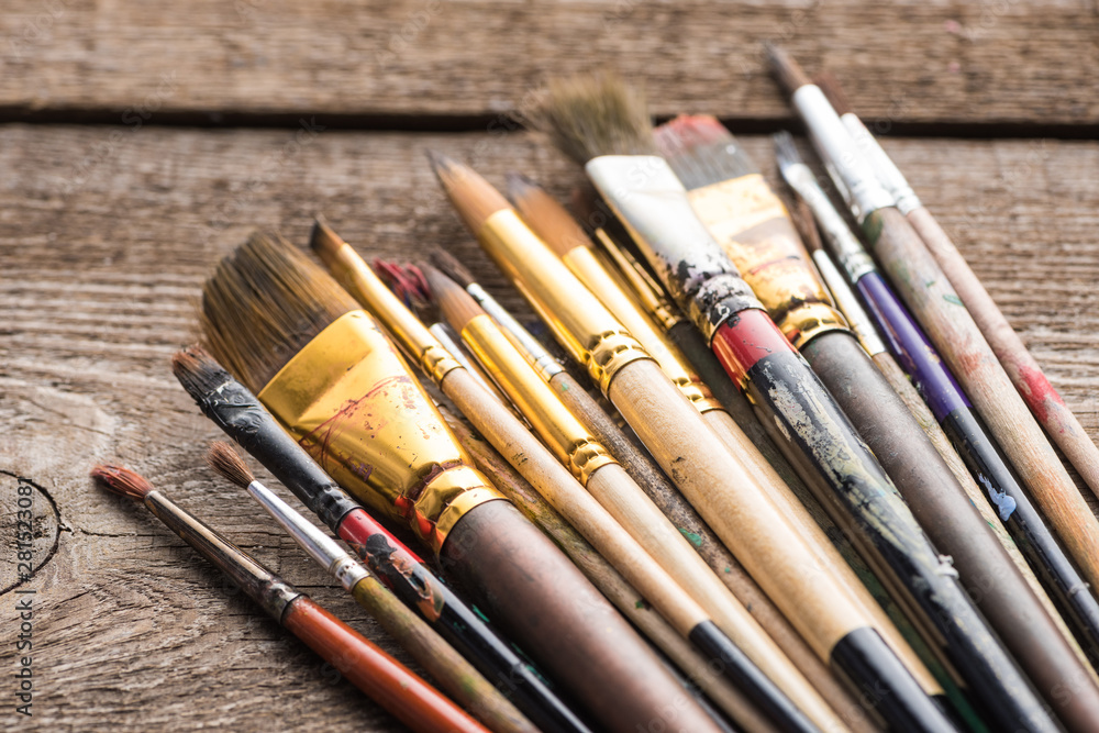 Fototapeta premium close up view of aged paintbrushes on wooden brown surface