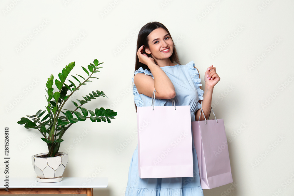 Beautiful young woman with blank paper bags near white wall, space for text Beautiful young woman with blank paper bags near white wall, space for text