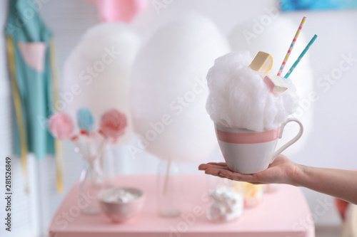 Woman holding cup with cotton candy dessert on blurred background, closeup. Space for text