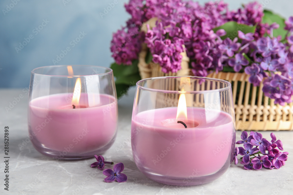 Burning wax candles in glass holders and lilac flowers on grey table Burning wax candles in glass holders and lilac flowers on grey table