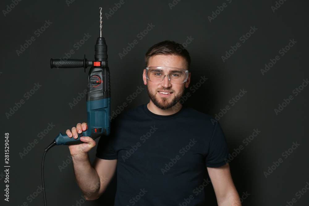 Young working man with rotary hammer on dark background Young working man with rotary hammer on dark background