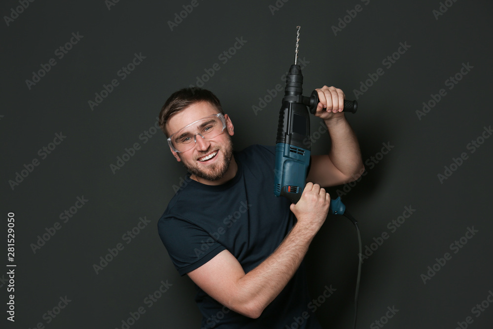 Young working man with rotary hammer on dark background Young working man with rotary hammer on dark background