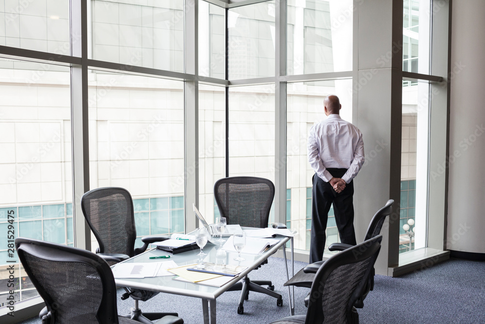 Rear view of businessman looking through window in office Rear view of businessman looking through window in office