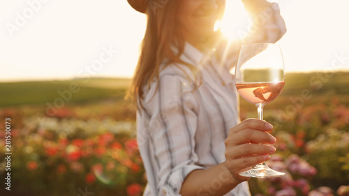 Woman with glass of wine in rose garden on sunny day, closeup