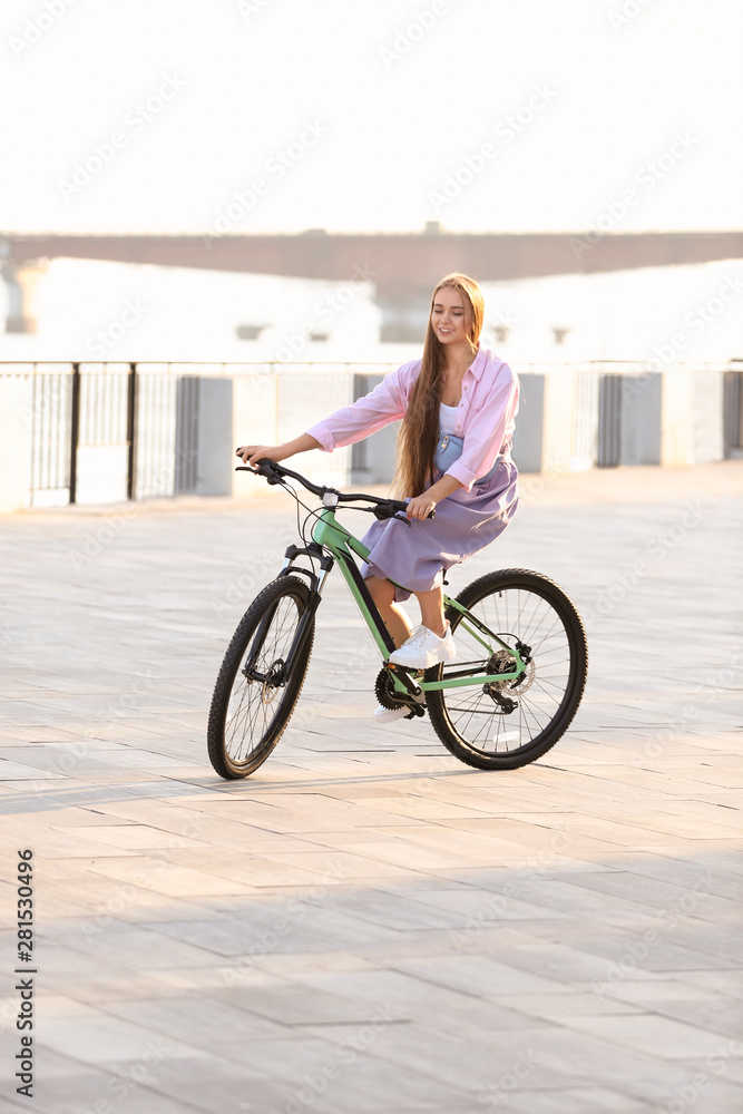 Fototapeta premium Young woman riding bicycle in city on sunny day