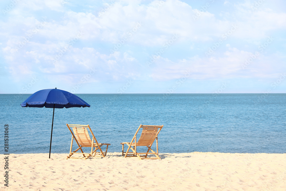 Empty wooden sunbeds and umbrella on sandy shore. Beach accessories