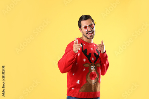 Happy man in Christmas sweater and party glasses on yellow background