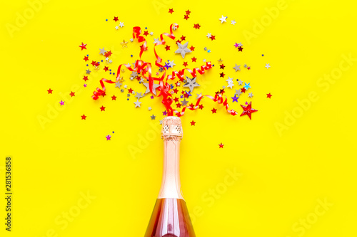 Party with champagne bottle and colorful party streamers on yellow background top view