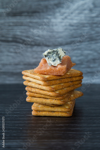 Delicious homemade quince paste served with creamy blue vein cheese and wheat crackers. On a dark background, nice contrast. Great combination of sharp cheese with sweet paste on a salty cracker. photo