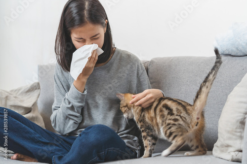 Diseases from pets concept. Woman is sneezing from fur allergy on the sofa and playing with her cat. photo