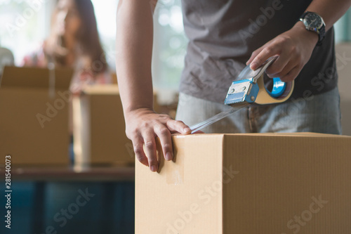 Concept young couple moving house. Close-up hand of man use tape sealing cardboard box. photo