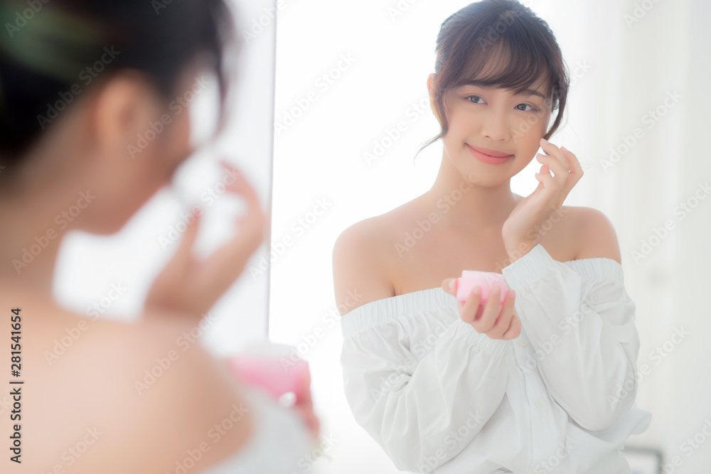 Beautiful portrait young asian woman applying cream moisturizer or lotion skin care cosmetic on face looking mirror, girl with treatment facial, health and wellness concept. Beautiful portrait young asian woman applying cream moisturizer or lotion skin care cosmetic on face looking mirror, girl with treatment facial, health and wellness concept.