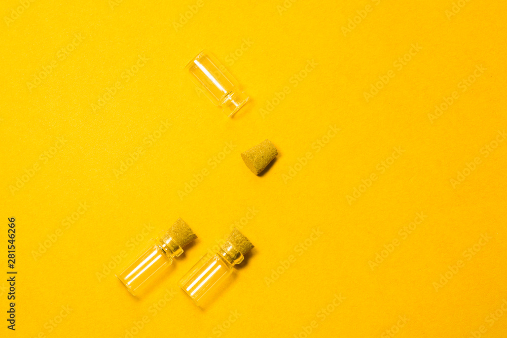 Naklejka premium Empty little bottles with cork stopper isolated on yellow. transparent containers. test tubes. copy space