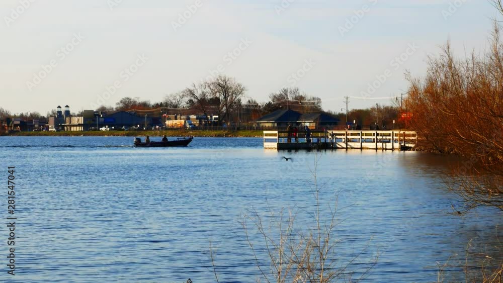 People in a fishing boat and on a pier on Lake Bemidji near the Mississippi River on the morning of Minnesota Fishing Opener with buildings and traffic on far shore. People in a fishing boat and on a pier on Lake Bemidji near the Mississippi River on the morning of Minnesota Fishing Opener with buildings and traffic on far shore.
