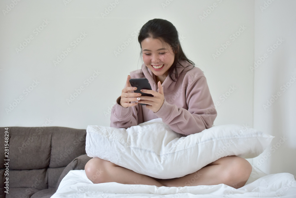 Young Asian Women holding mobile smart phone sitting on bed Young Asian Women holding mobile smart phone sitting on bed