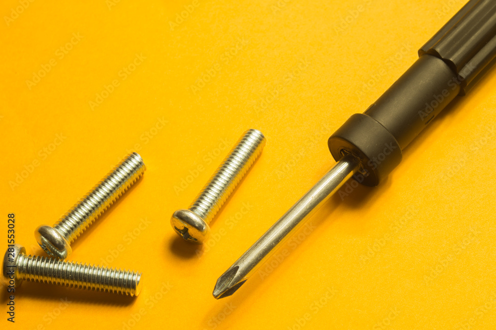 Screws and screwdriver on a yellow background Screws and screwdriver on a yellow background